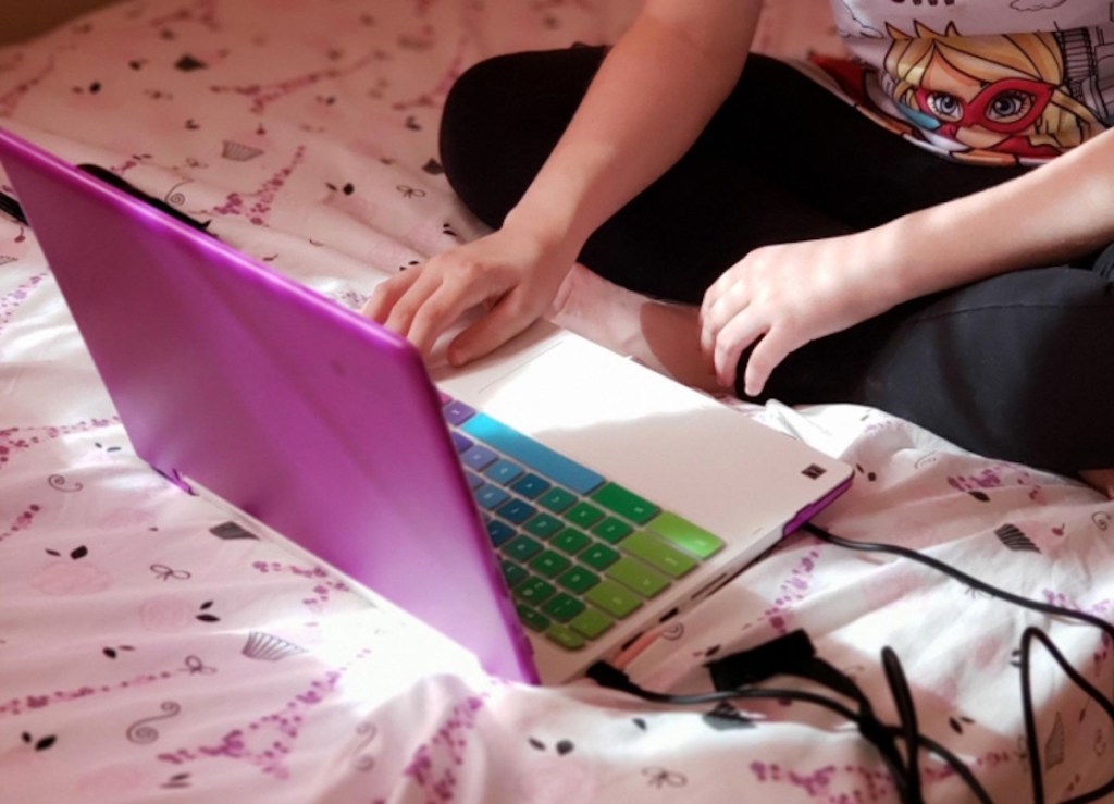 girl typing on purple laptop on bed with colorful keyboard