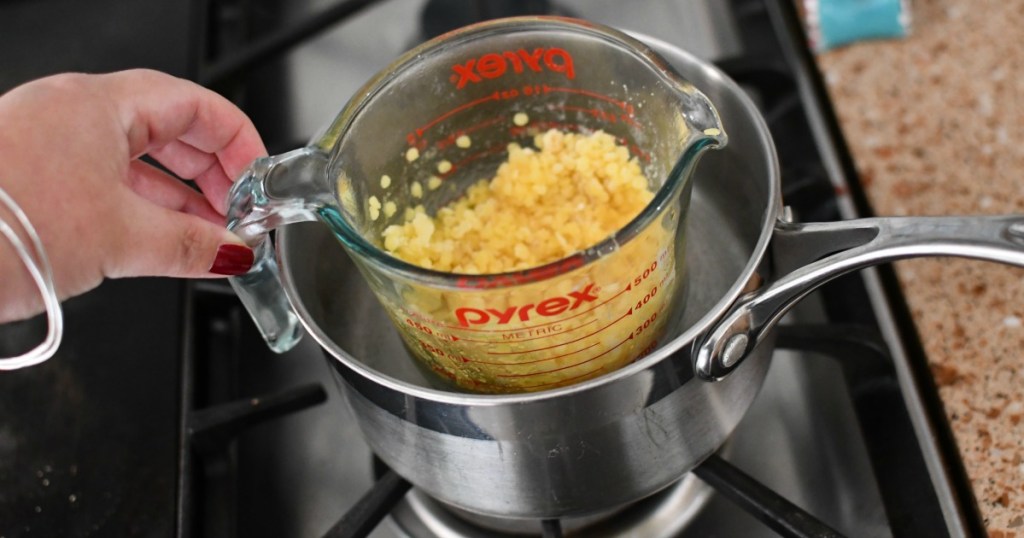 making a double boiler with measuring cup inside pot of water