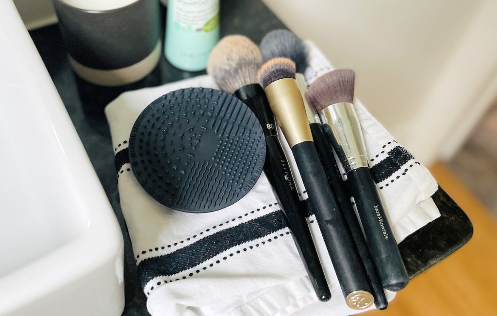 makeup brushes and black silicone mat laying on stripe towel in bathroom