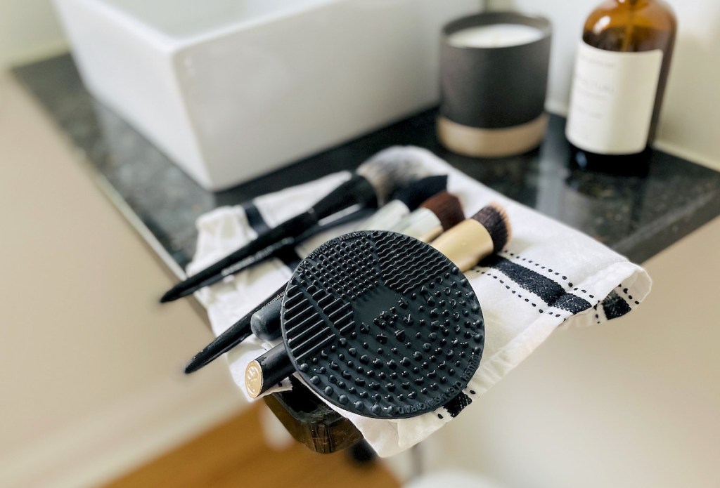makeup brushes and black silicone mat on stripe towel on bathroom counter 