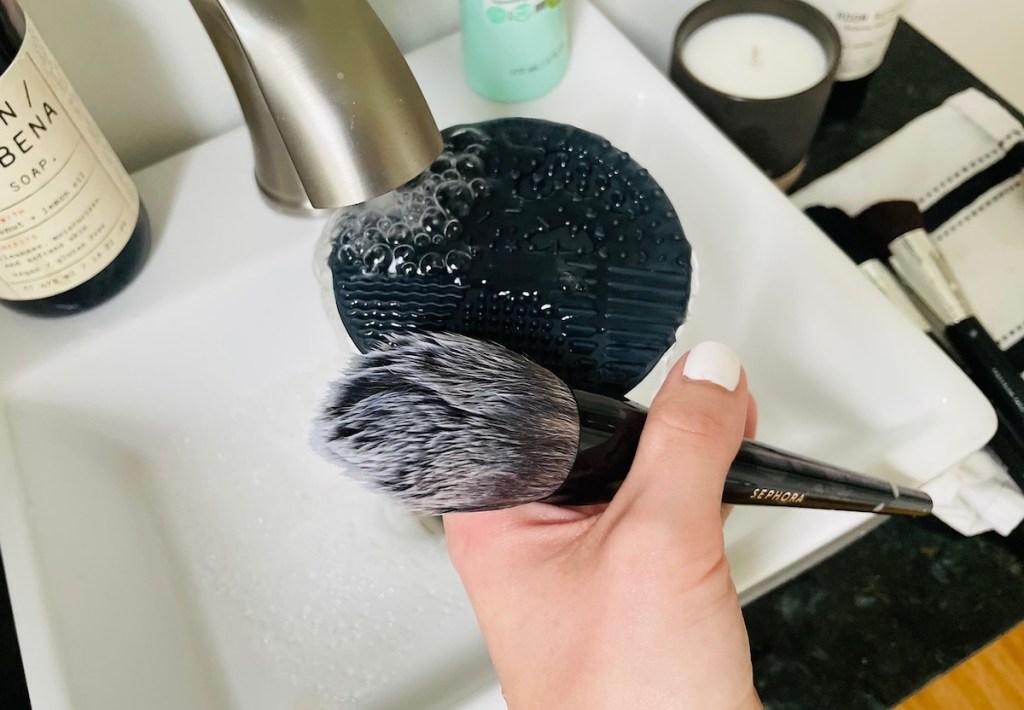 black silicone mat and makeup brush under running faucet in bathroom sink