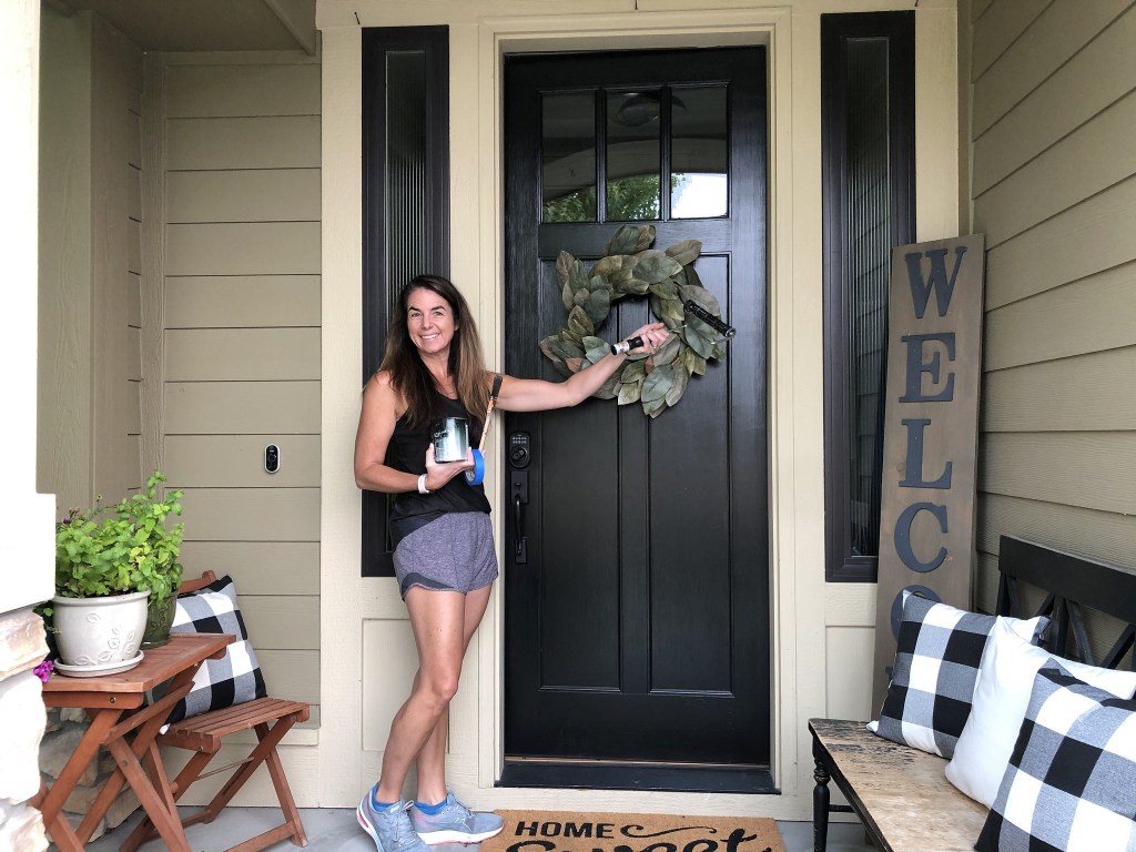 woman standing by black painted front door with wreath