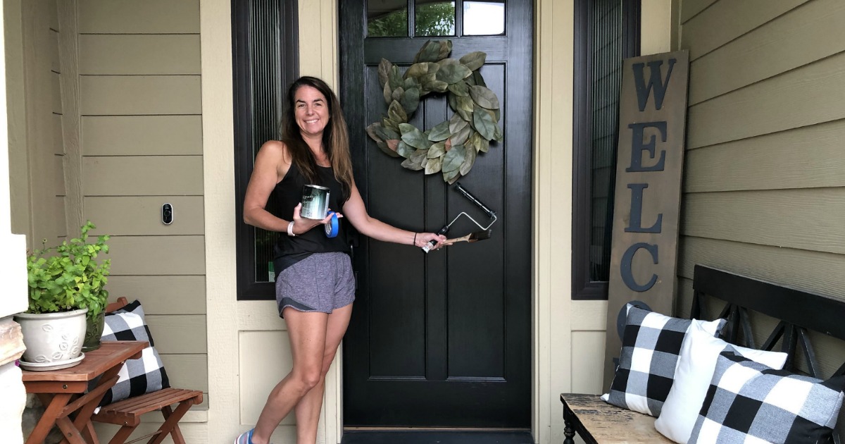 woman painting door black holding can of paint