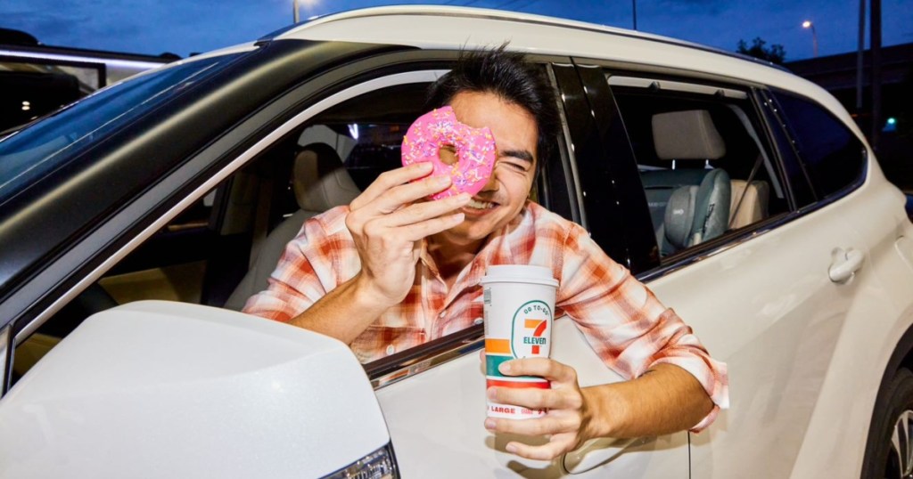 man holding coffee and doughnut out car window