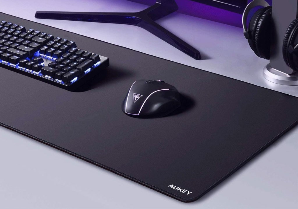 large black gaming mousepad under a keyboard and mouse on grey desk