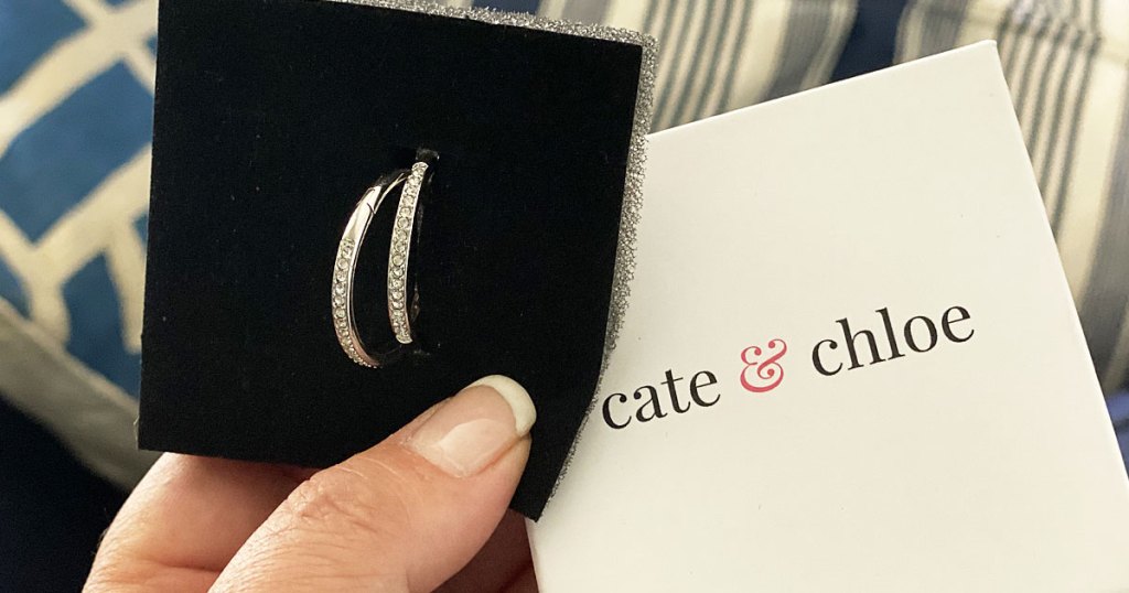 woman holding a pair of white gold sparkly hoop earrings with the cate & chloe jewelry box they're packaged in