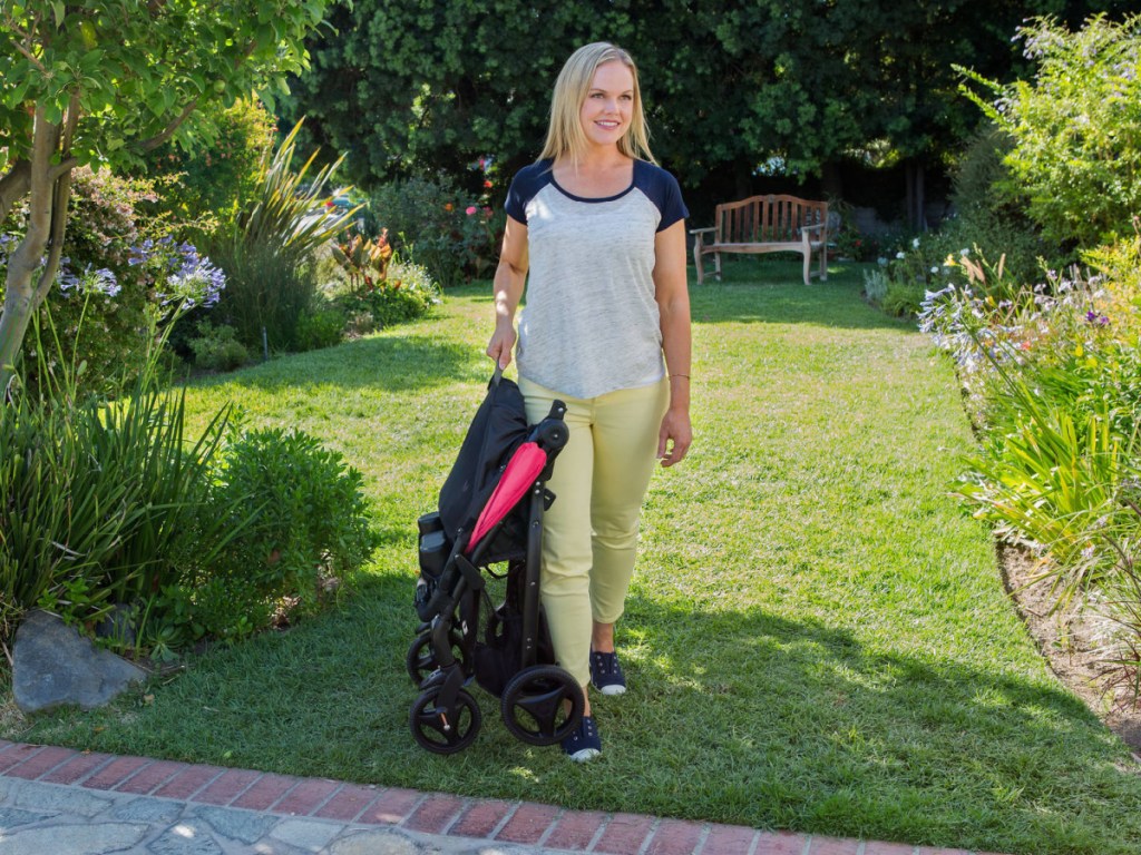 woman outside carryng a folded up black and bright pink stroller