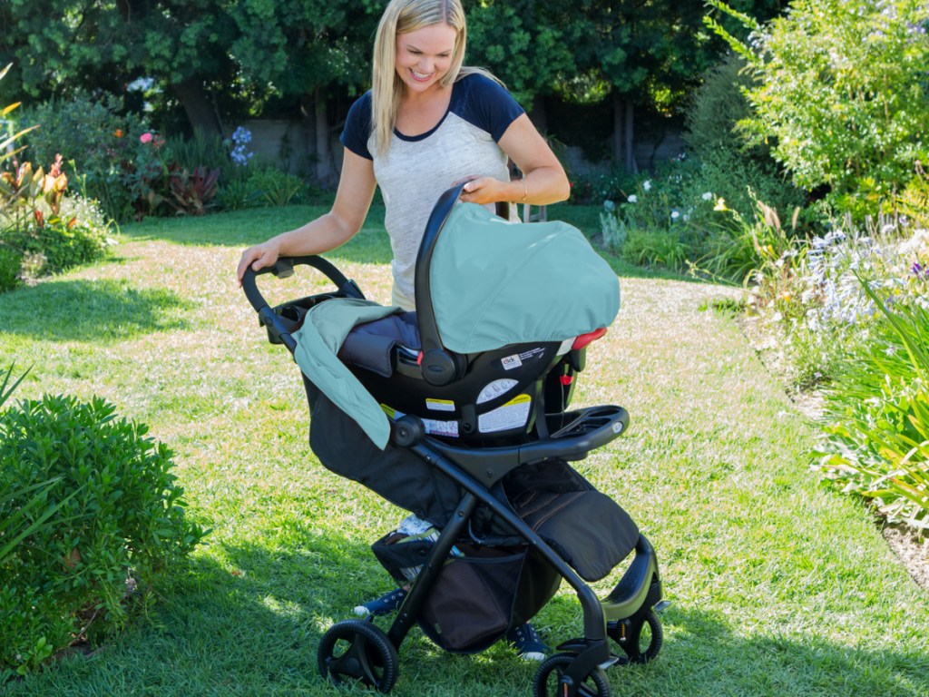 woman standing outside over a bright pink and black care seat stroller system 