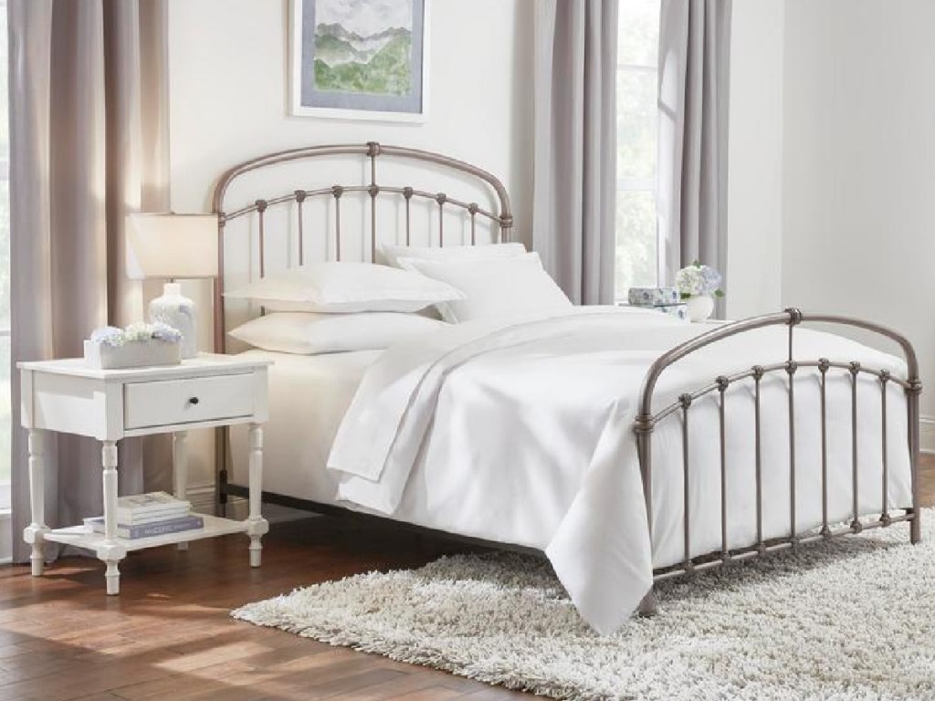 Pewter colored metal bed with white bedding surrounded by white bedroom furniture