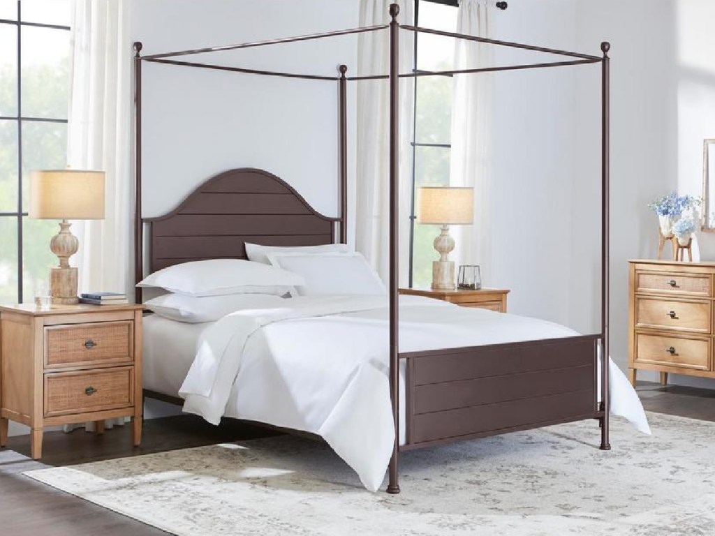 bronze colored metal canopy bed with white bedding in a bedroom with brown bedroom furniture