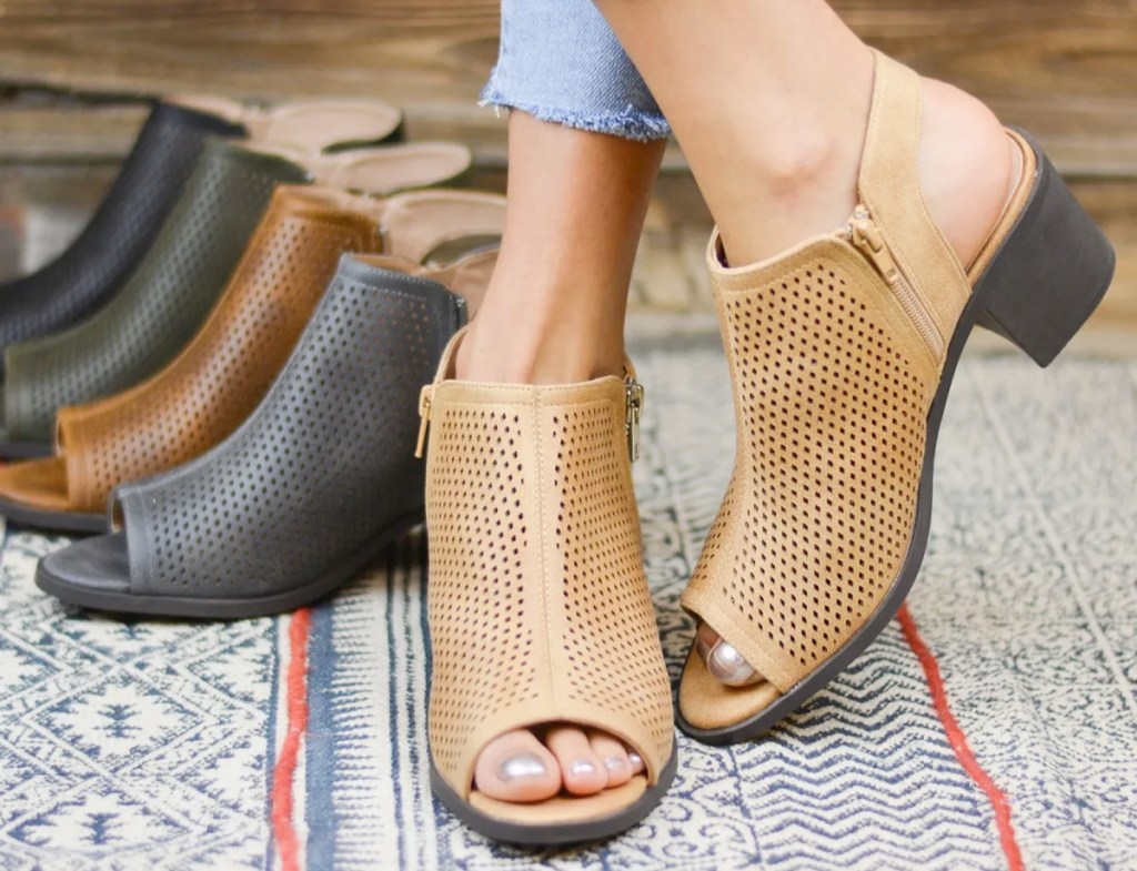 woman wearing a pair of tan peep-toe booties with other colors of booties behind her