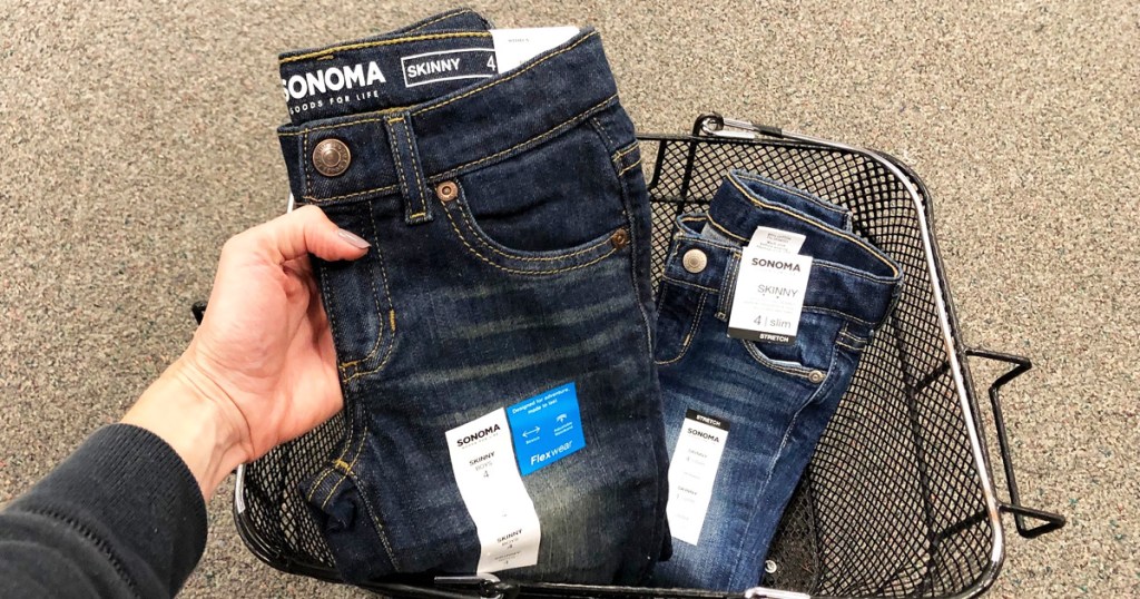 woman holding up pair of sonoma girls jeans from black shopping basket on floor