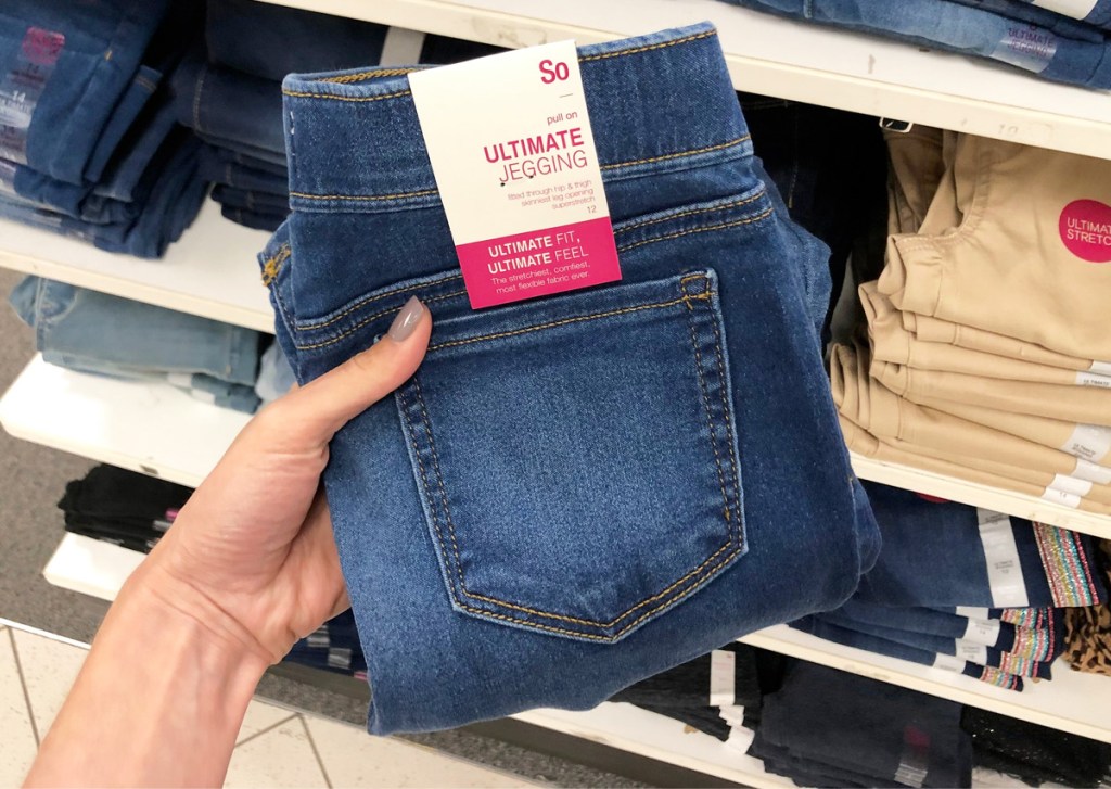 woman holding up a folded pair of SO brand girls jeggings