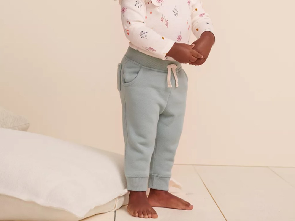 toddler girl wearing light green colored joggers next to a pillow on the floor