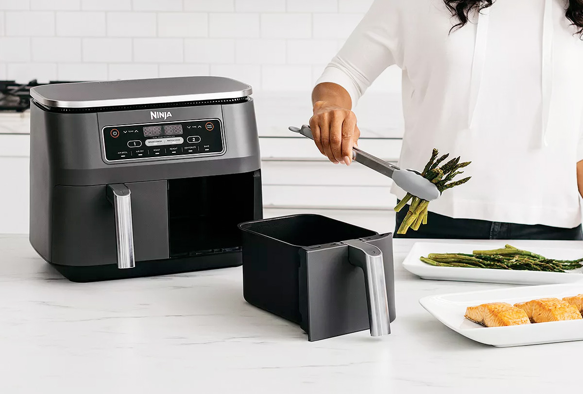 woman using a Ninja Foodi air fryer with two frying baskets to cook asparagus and salmon