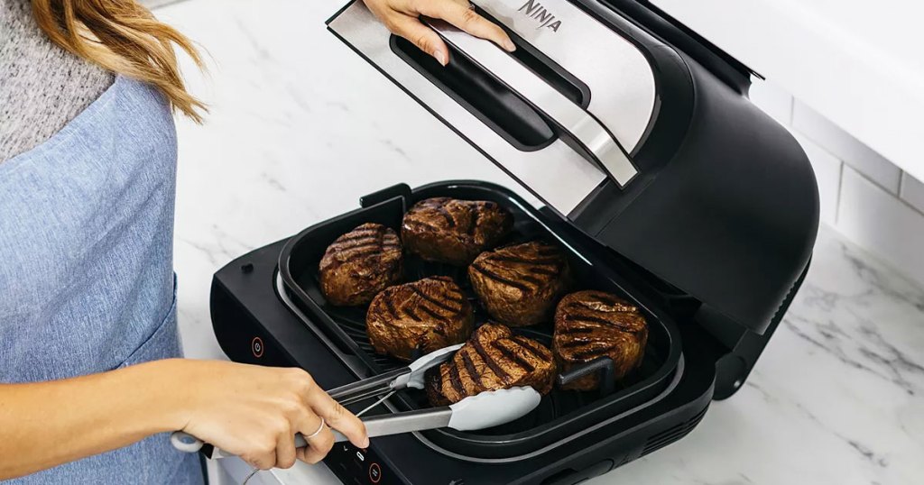 person using a pair of tongs to remove grilled steaks from Ninja Foodi grill