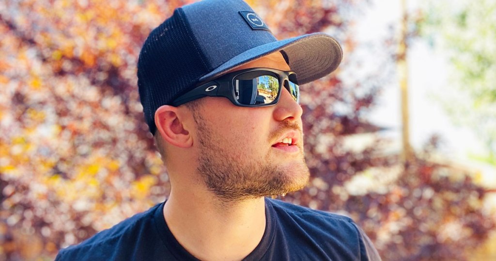 man standing outside wearing grey hat, black oakley sunglasses, and black t-shirt