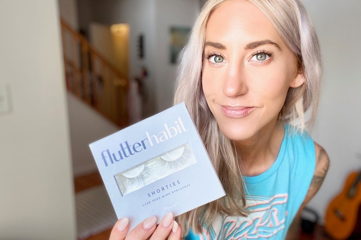 A woman holding a box of shortie eyelashes and wearing them