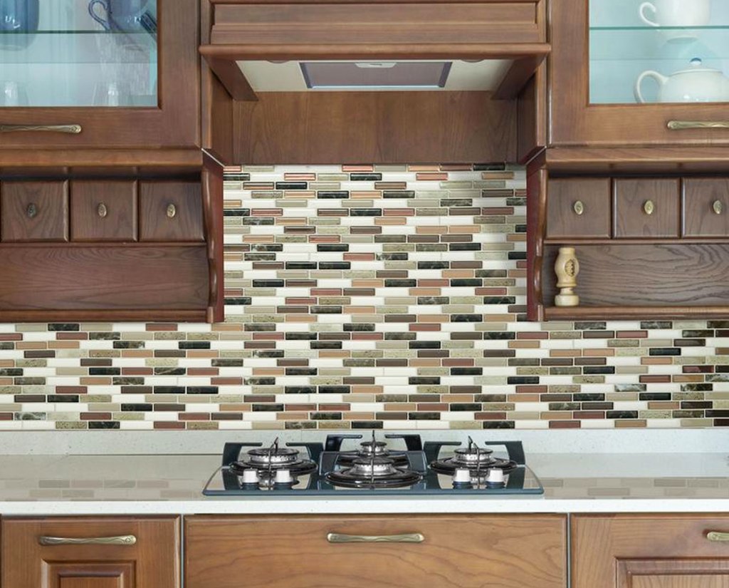 brown and cream colored peel and stick tile backsplash on wall under brown wood cabinets in front of stove