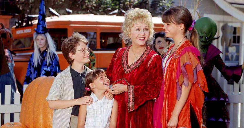 A woman and 3 children smiling while others in Halloween costumes surround them