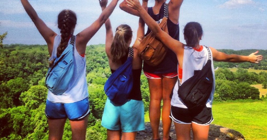 girls looking at moutains with arms raised and wearing backpacks