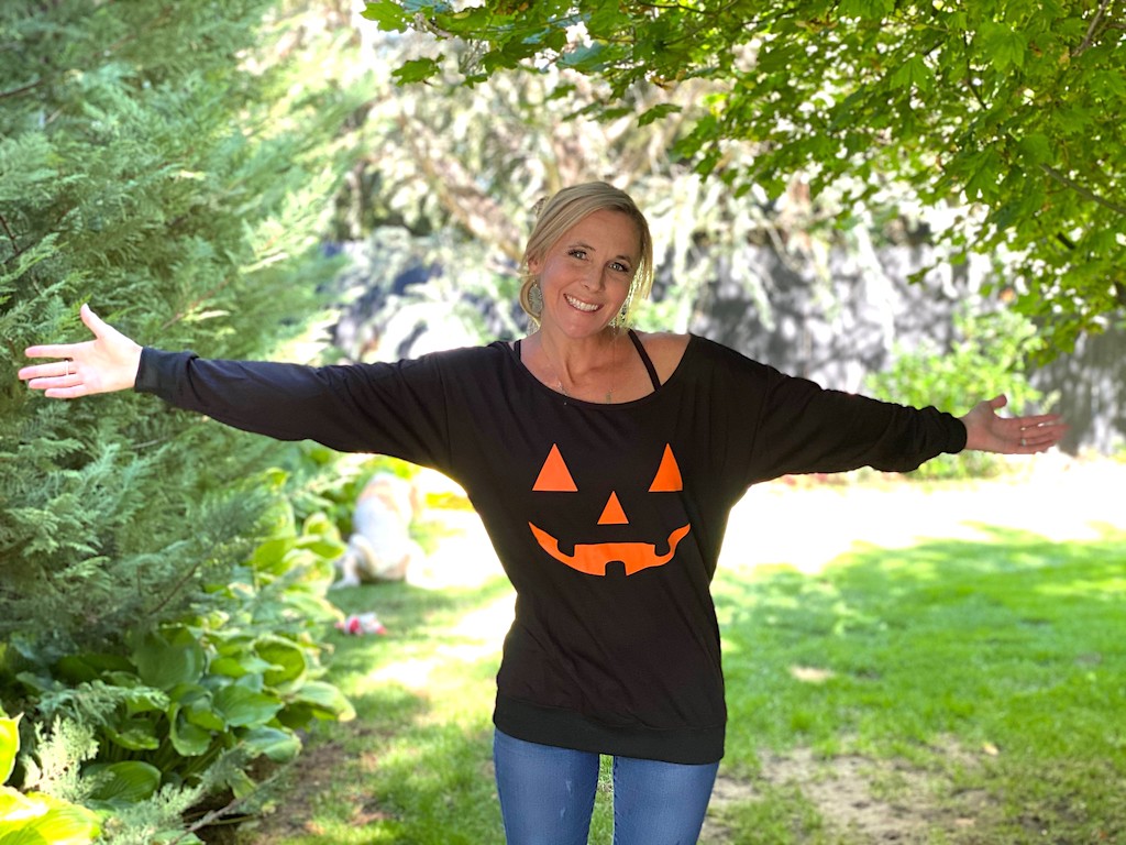 woman in pumpkin sweatshirt with arms out outside 