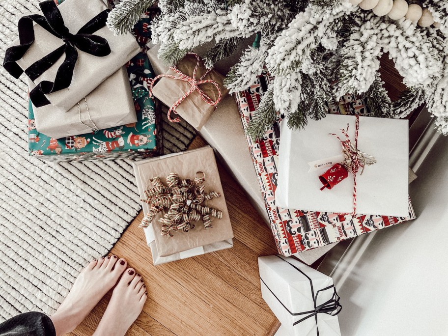 feet standing in front of flocked christmas tree with 4 gift rule presents on floor