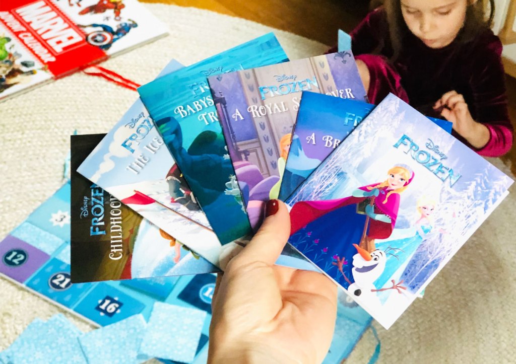 person holding up a variety of books that come inside the disney frozen storybook advent calendar