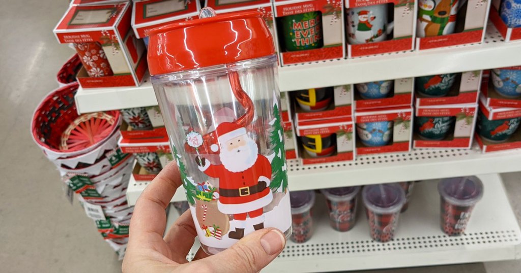 person holding up Santa print kids tumbler with red swirly straw inside in front of other christmas mugs on display at dollar tree