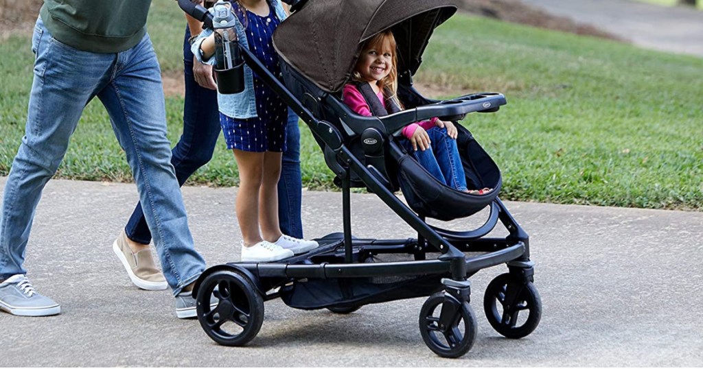 family walking with one child standing and one sitting in double stroller