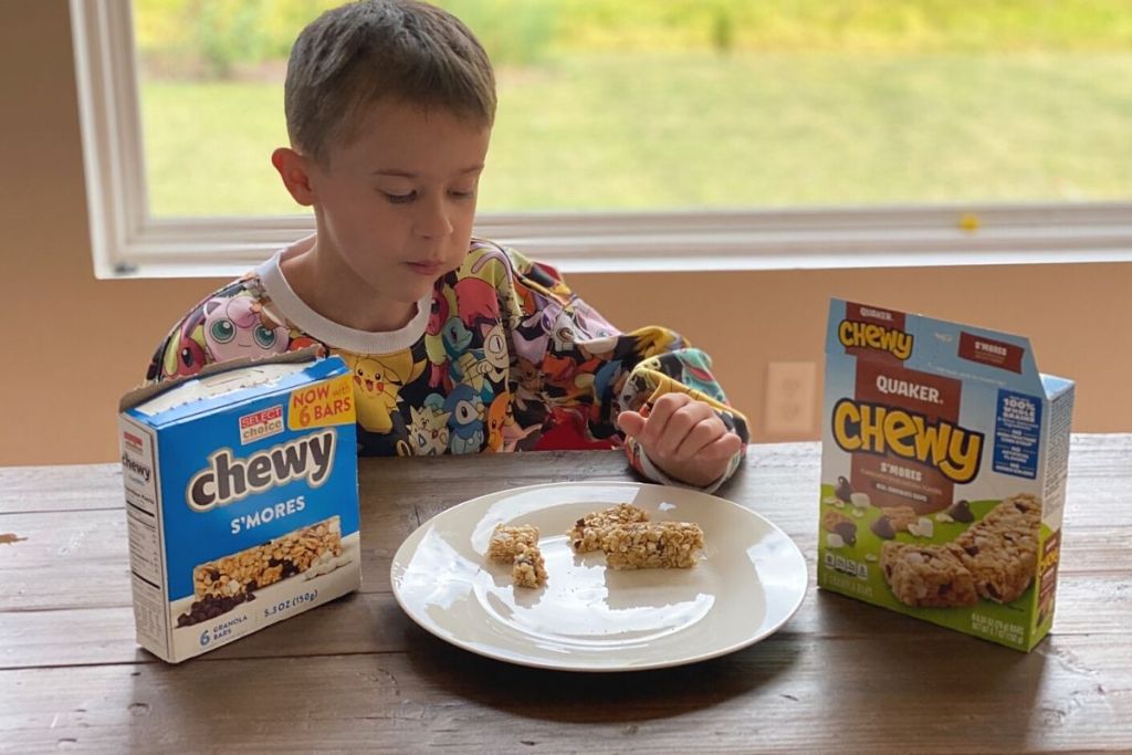 A boy eating granola bars on a plate next to the boxes