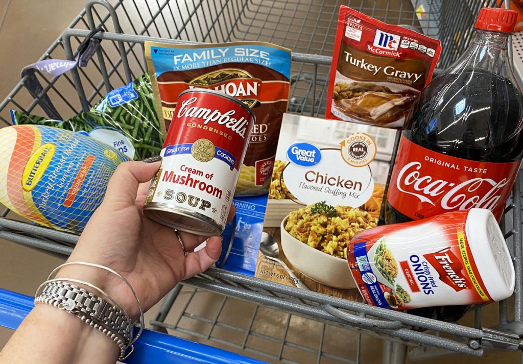 walmart shopping cart full of thanksgiving dinner items with woman holding up can of campbell's cream of mushroom soup