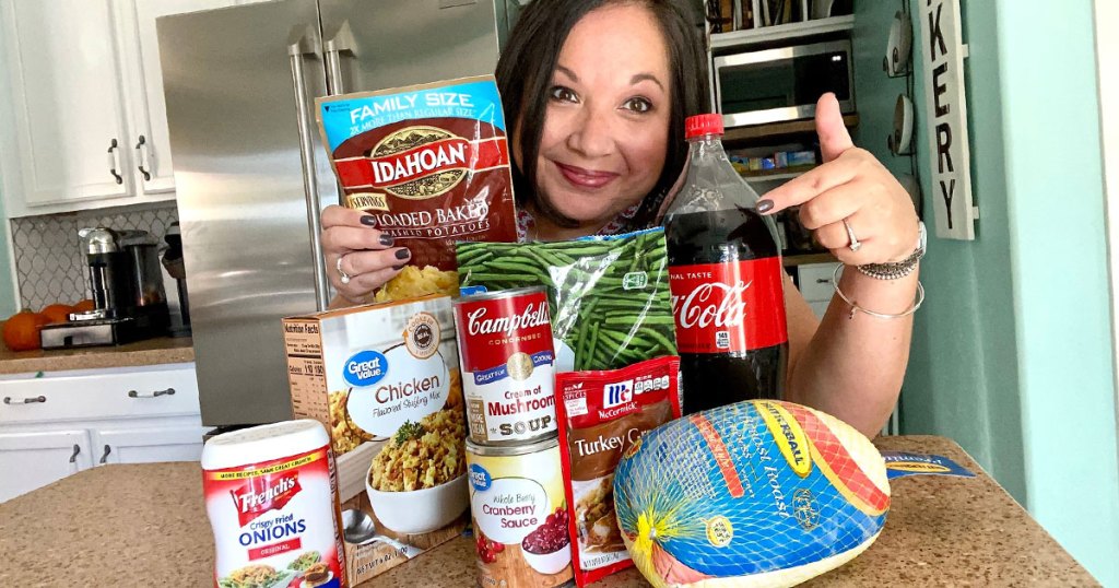 woman holding instant potatoes and pointing at thanksgiving dinner ingredients on kitchen counter in front of her