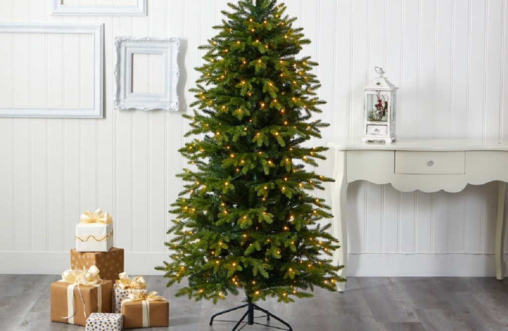 large lit christmas tree next to presents and a white console table