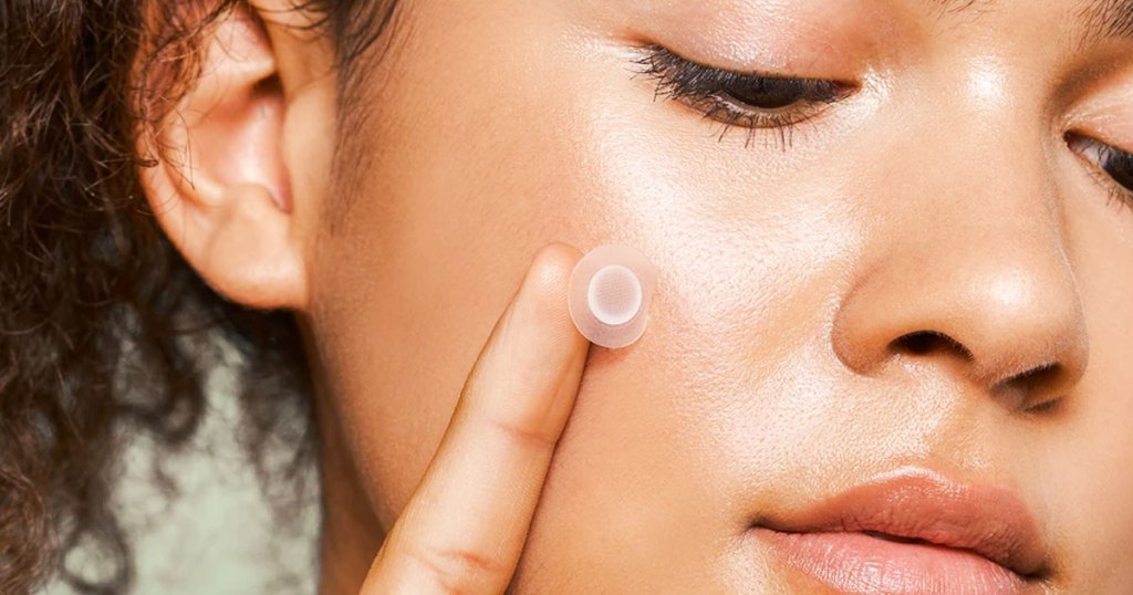 woman applying a pimple healing patch to her face