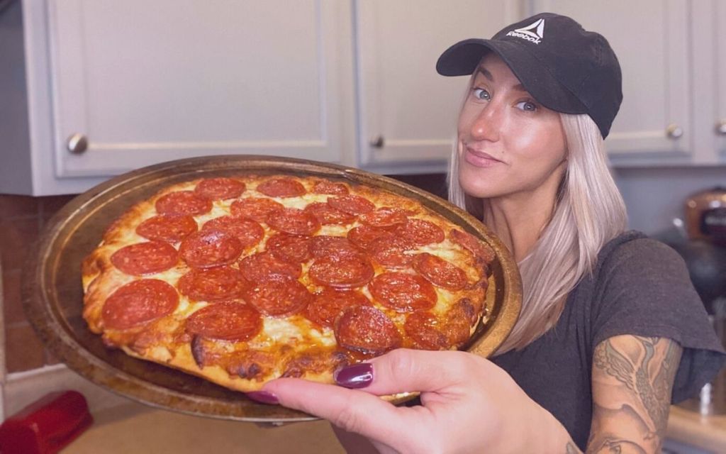 A woman holding a screamin sicilian pizza 