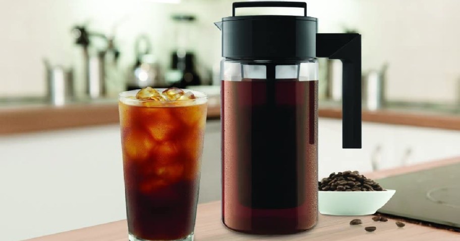 Takeya Patented Deluxe Cold Brew Coffee Maker filled with cold brew coffee next to a glass with coffee and ice cubes