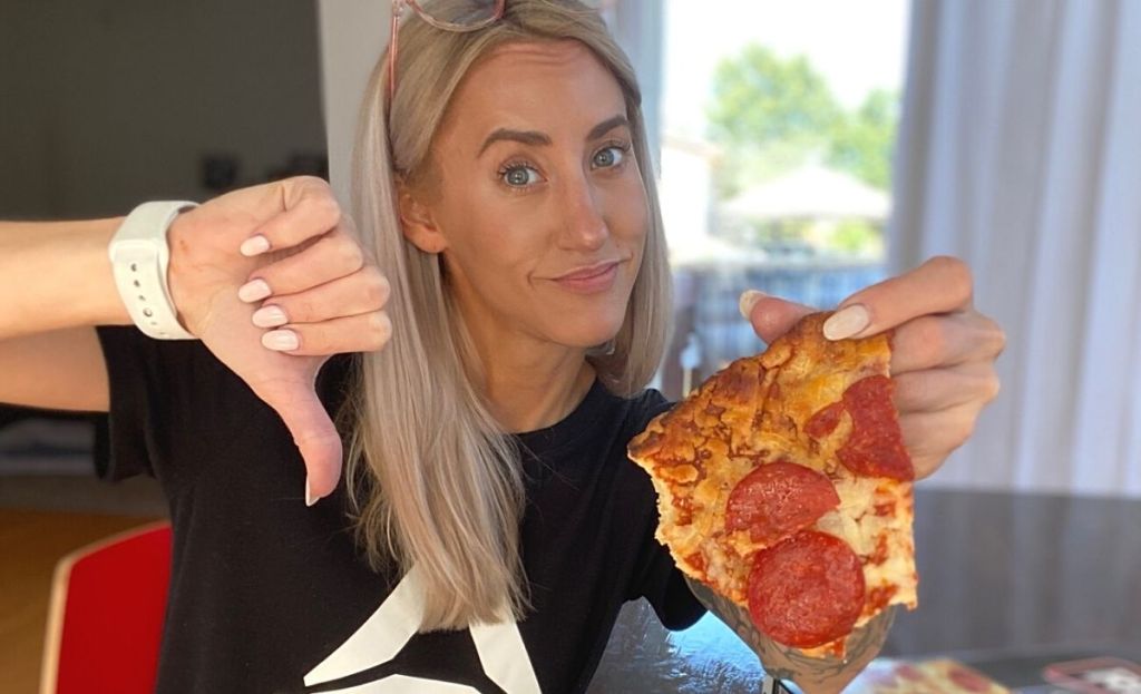 A woman holding a piece of pizza and making a thumbs down gesture