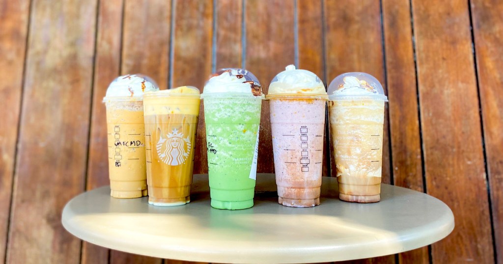 row of various kinds of starbucks drinks on table in front of wood wall