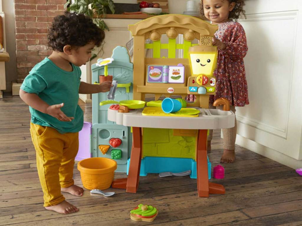 two toddlers playing with a fisher price kitchen