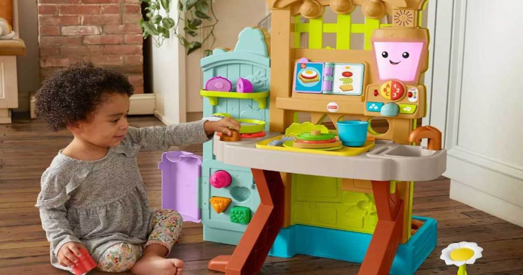 toddler sitting on the floor playing with fisher price garden kitchen