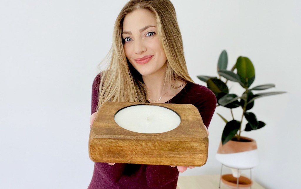 woman holding out candle with plant in background