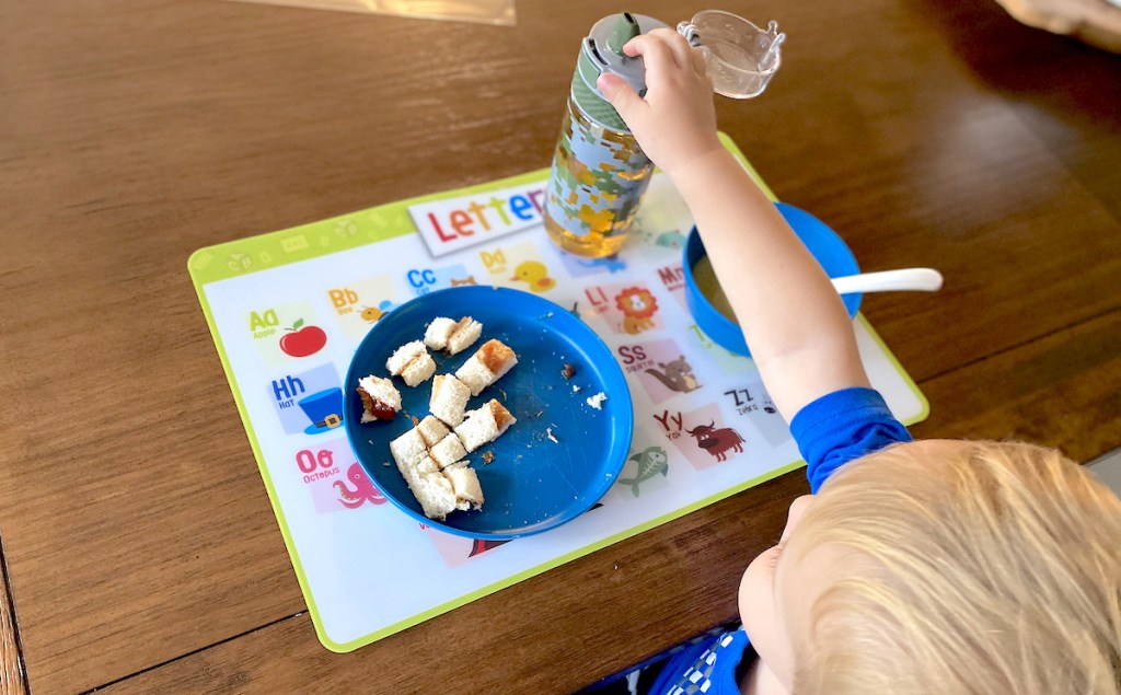 toddler kid grabbing sippy cup with food on blue plate