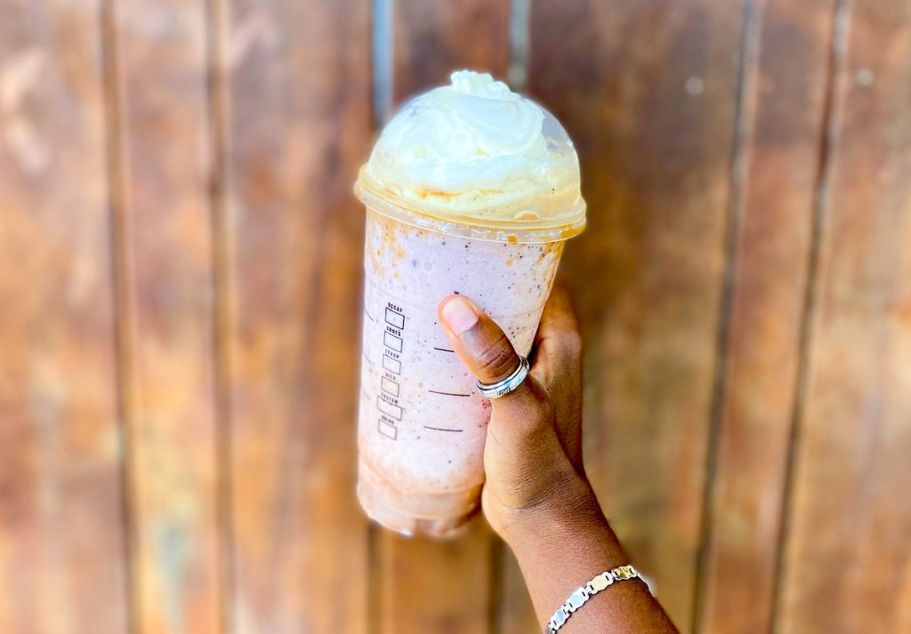 hand holding a pink frappuccino in front of wood wall