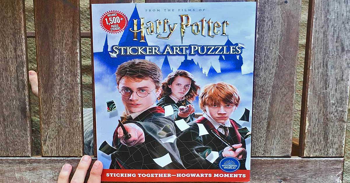 hand holding a harry potter sticker book against a wooden slat fence