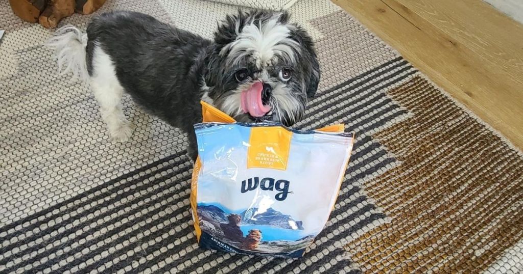 fluffy gray and white dog licking his face in front of wag dog food bag