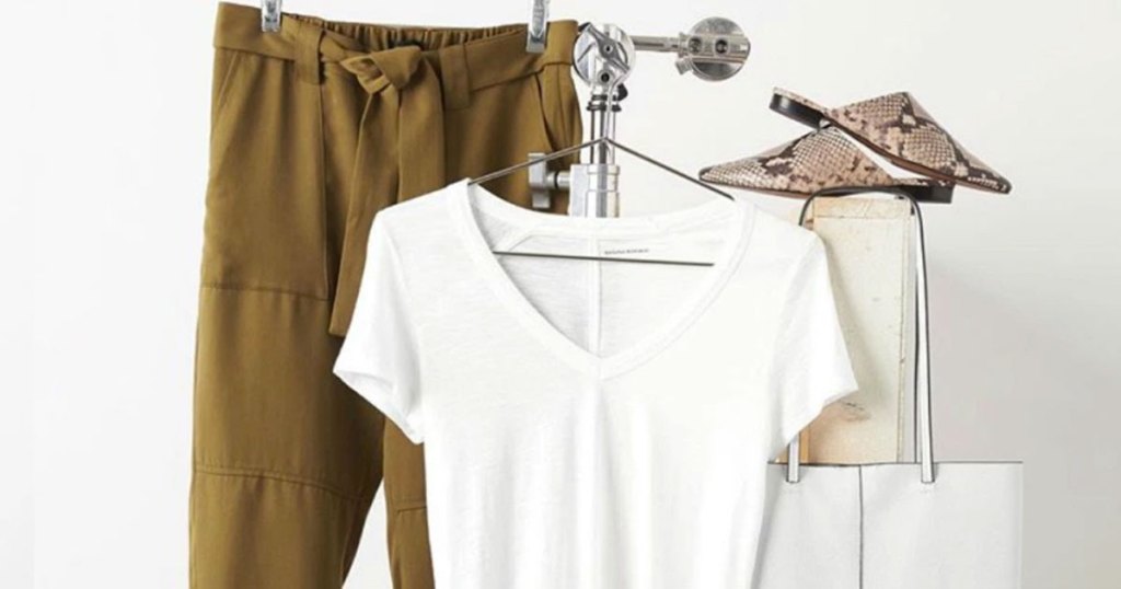 white tee and brown tie-waist pants hanging on a clothing rack with pair of shoes and white bag