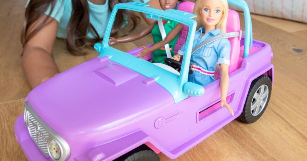 girl playing with purple toy car with two dolls inside