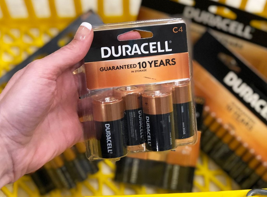 woman holding up 4-pack of duracell C batteries in front of other types of duracell batteries in yellow shopping basket