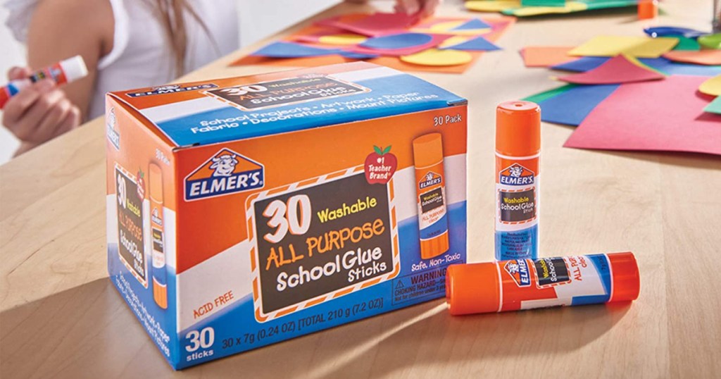 box of glue sticks on glue sticks on table with kids doing crafts